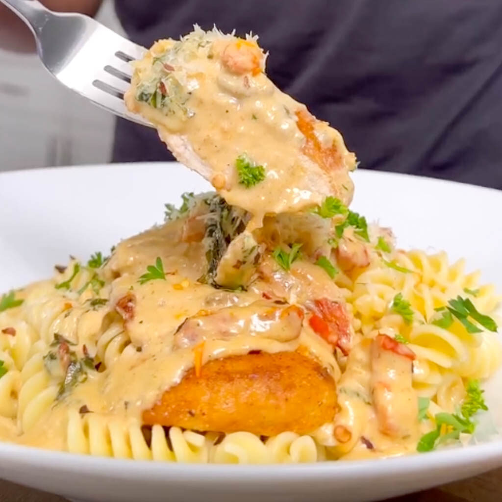 Bowl of pasta noodles with creamy sauce and crispy chicken with a fork holing up a large slice of the chicken with sauce on it