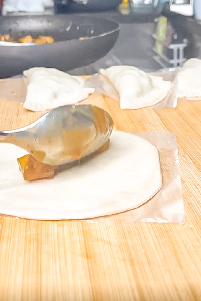 a spoon placing apple filling at the center of an empanada