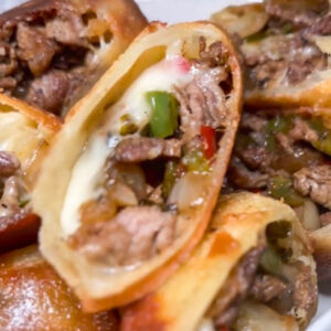 close up of inside of a cheesesteak egg roll on a plate with other egg rolls