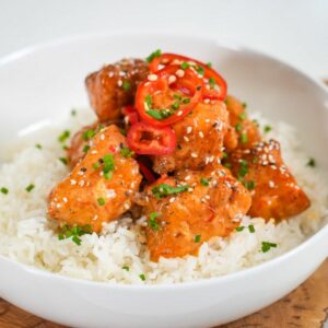 bang bang salmon bites over sprinkled with sesame seeds and green onions served over a bed of white rice