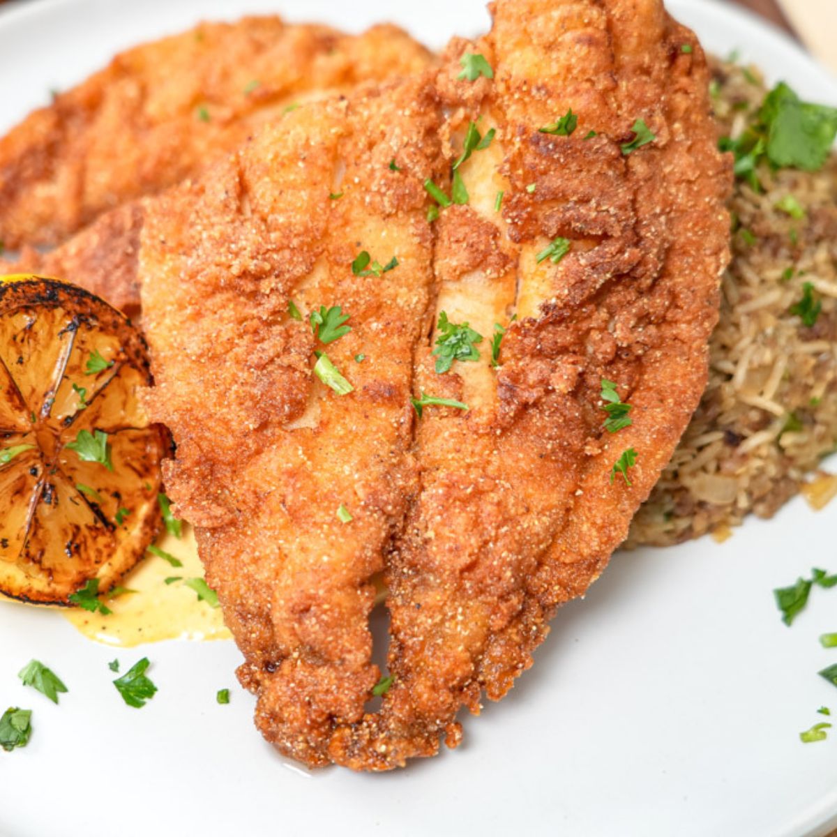 fried flounder sitting over a bed or rice with a charred lemon wedge on the side