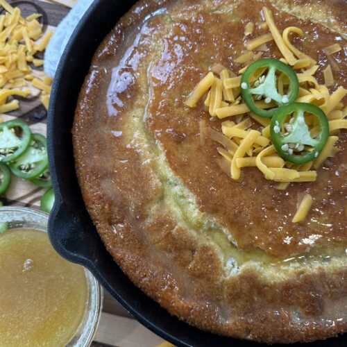 Fresh jalapeno cheddar cornbread with jalapeno slices and shredded cheese as garnish on top. Honey butter drizzled on top and served on side.
