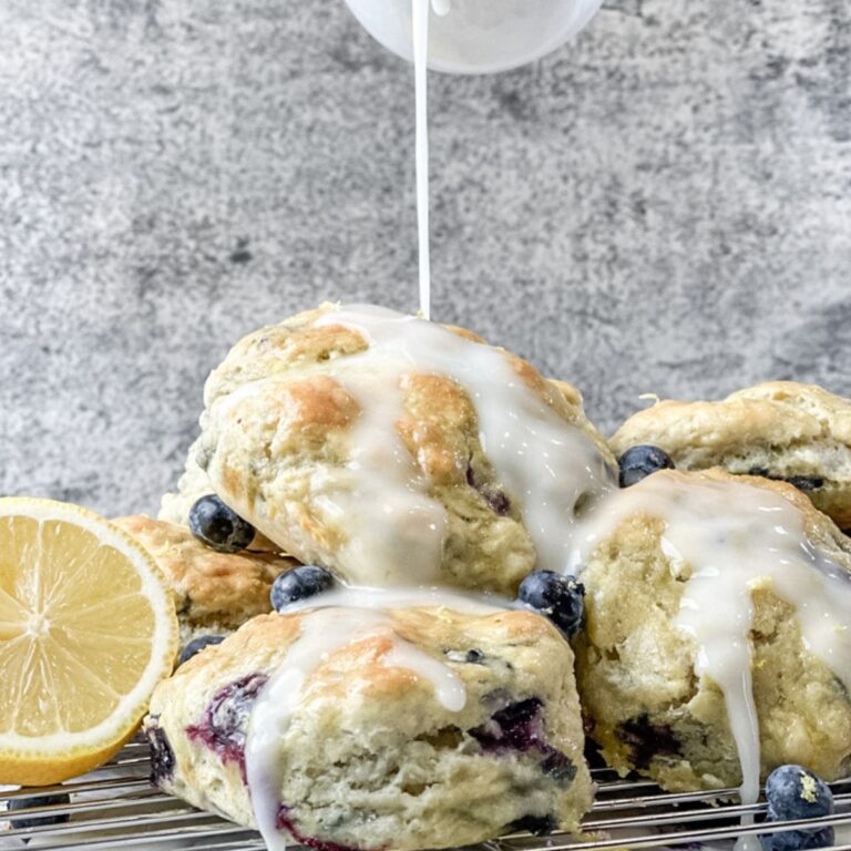 Lemon blueberry biscuits on a wire cooling rack being covered in fresh lemon glaze.
