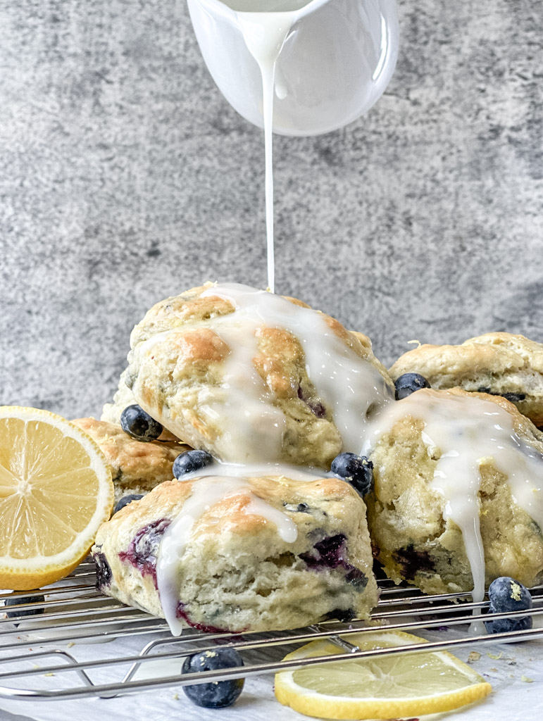 Lemon blueberry biscuits on a wire cooling rack being covered in fresh lemon glaze.