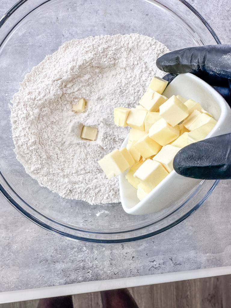 Ice cold butter cut into cubes being mixed into all-purpose flour in a glass bowl for the biscuit dough.