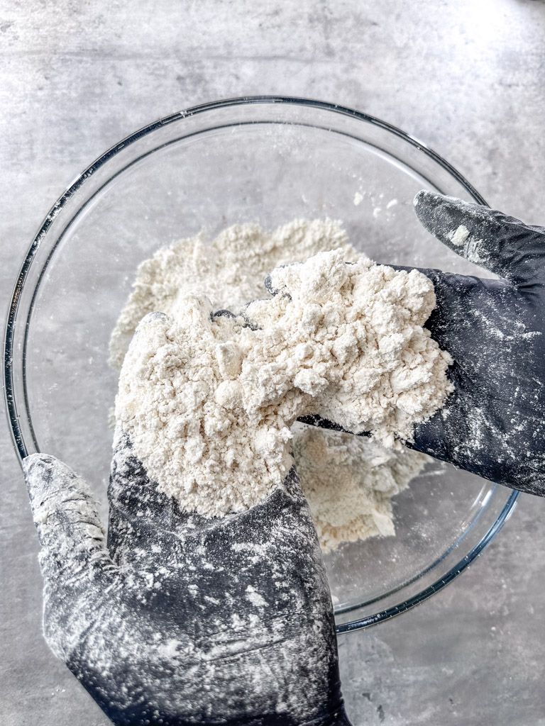 Chef using his hands to mix ingredients together to form the biscuit dough.