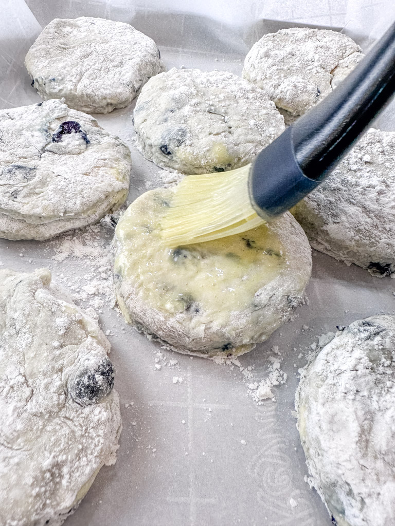 Egg wash being applied to uncooked blueberry biscuits