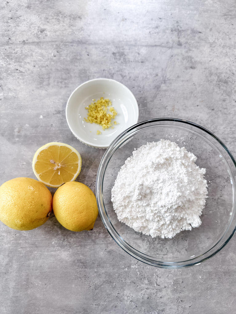 Ingredients for lemon glaze displayed on counter including confectioners sugar and fresh lemons.
