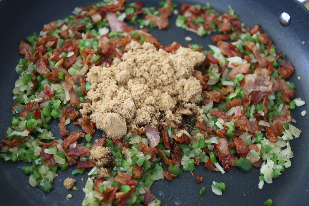 Brown sugar being added into the bacon jam in a frying pan.