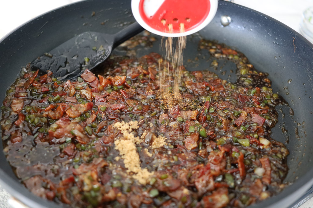 Spices are added to the bacon jam in a frying pan.