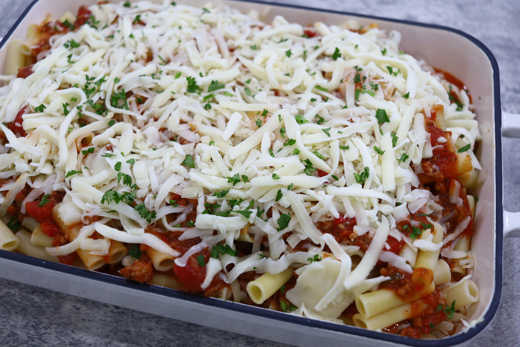 Uncooked baked ziti with mozzarella cheese and topped with parsley.