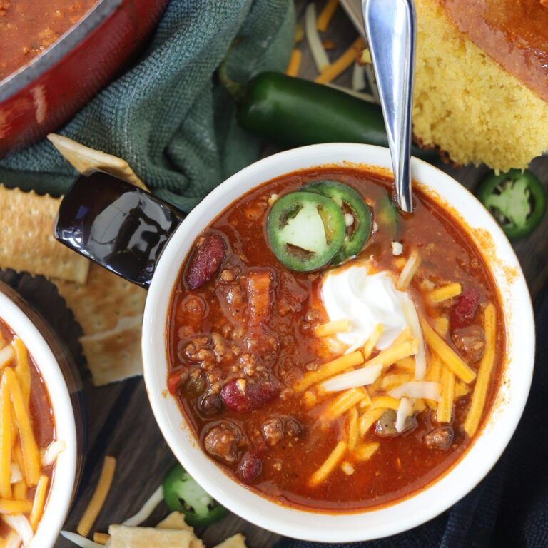 Chili in a bowl topped with shredded cheese, sour cream, and jalapenos.