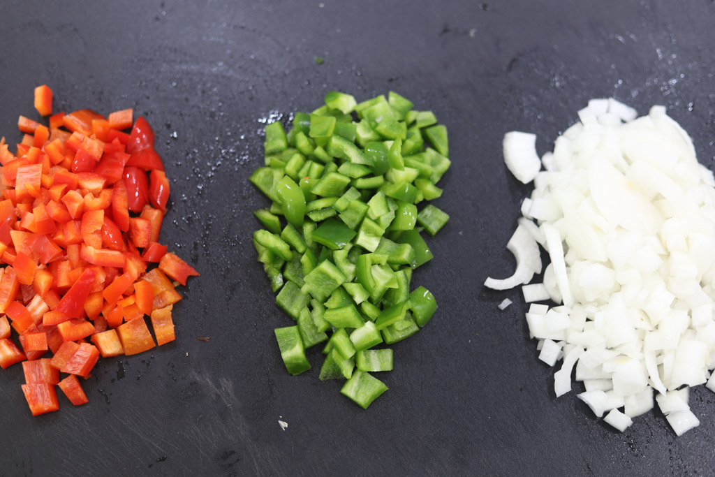 Diced onions, red peppers, and green peppers on a black counter.