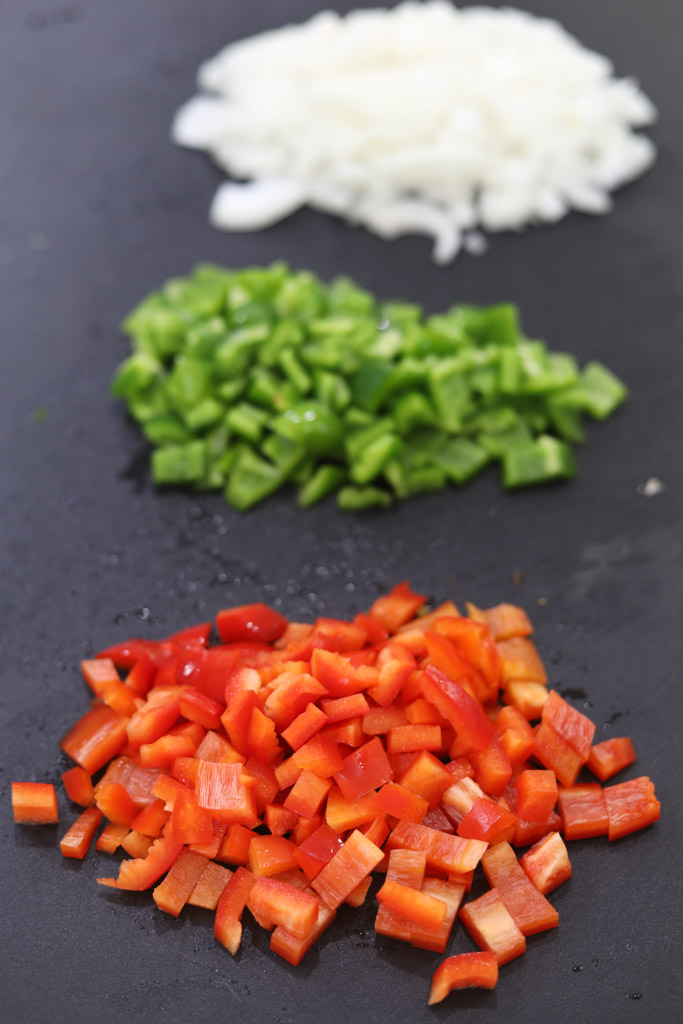 Diced onions, red peppers, and green peppers on a black counter.
