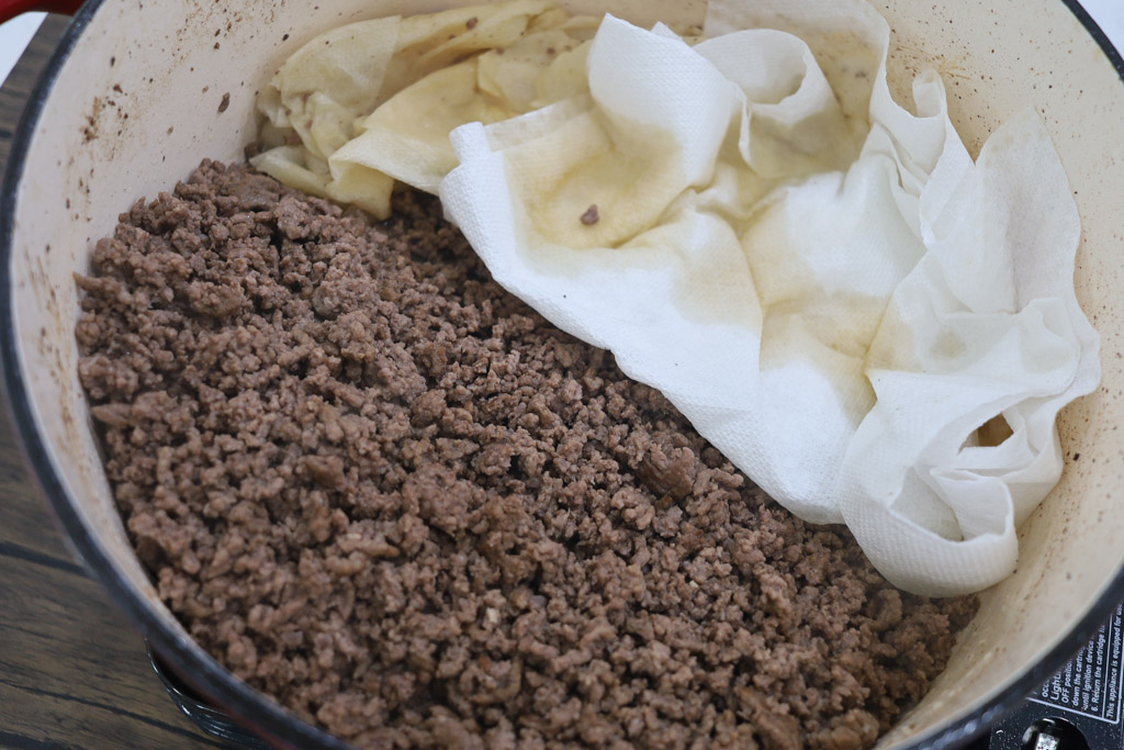 Putting paper towels in the dutch oven to soak up extra moisture from the cooked ground beef.