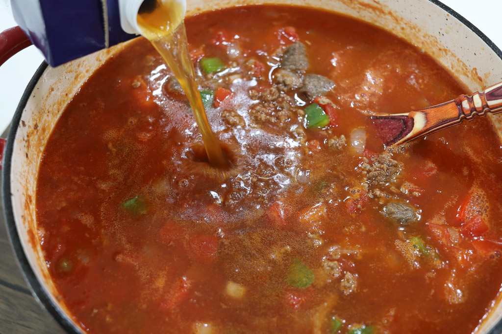 Adding the beef stock into the chili in a dutch oven.