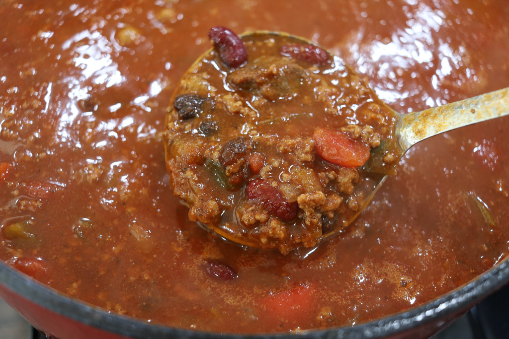 Chili in a dutch oven being shown close up in a ladle.