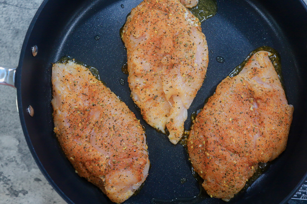 Seasoned, uncooked boneless skinless chicken breasts being pan seared.