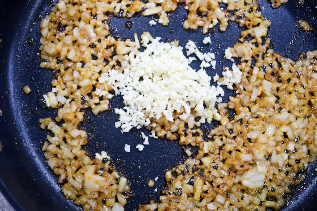 garlic and onions being cooked in a pan with oil.