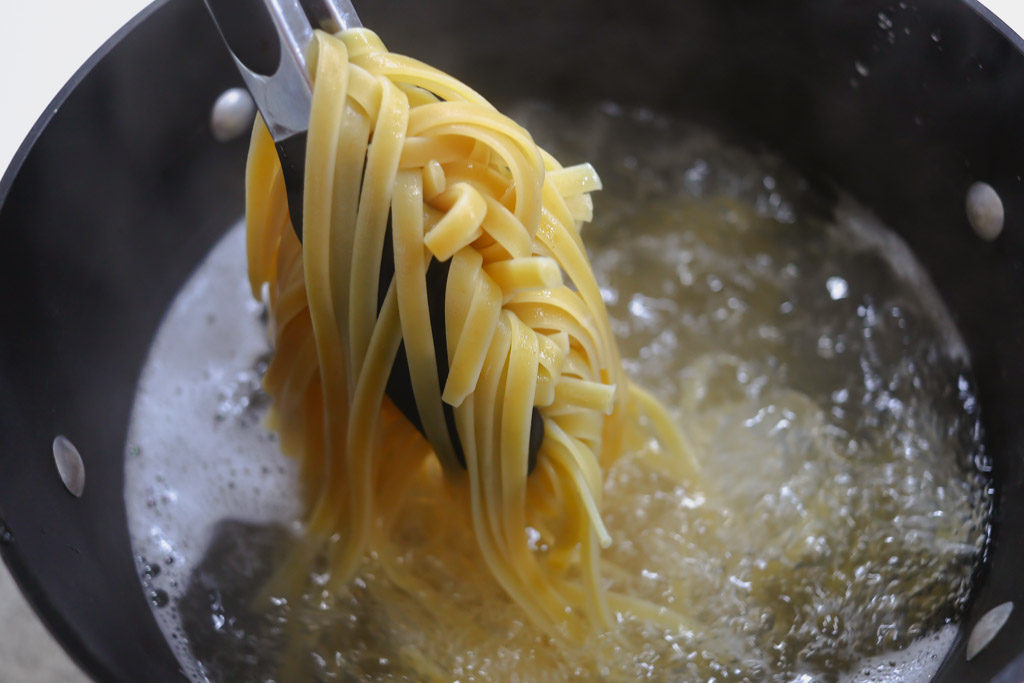 Fettuccine noodles being cooked in a pot of boiling water.