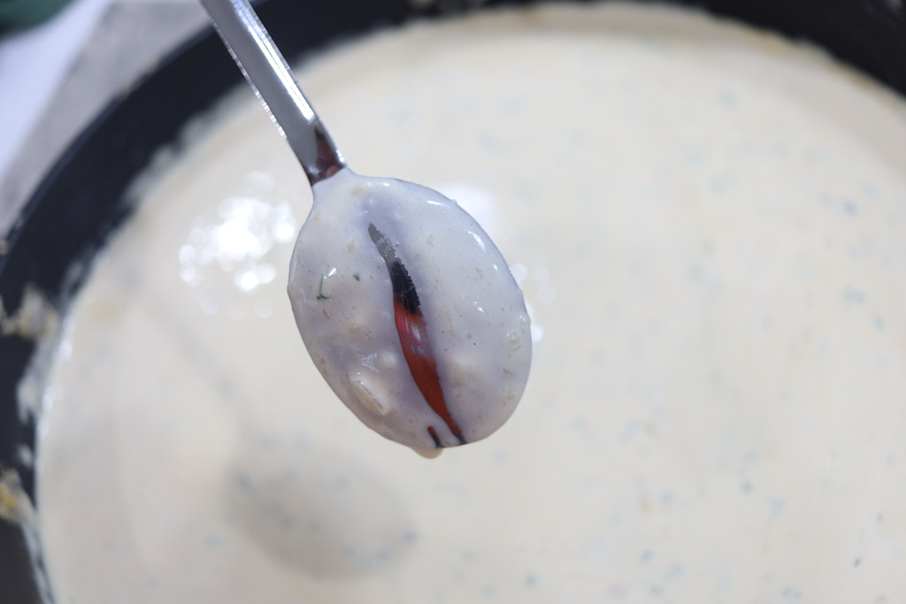 Alfredo sauce cooking in a pot. A spoon is being dipped into the sauce to show the viscosity of the sauce.