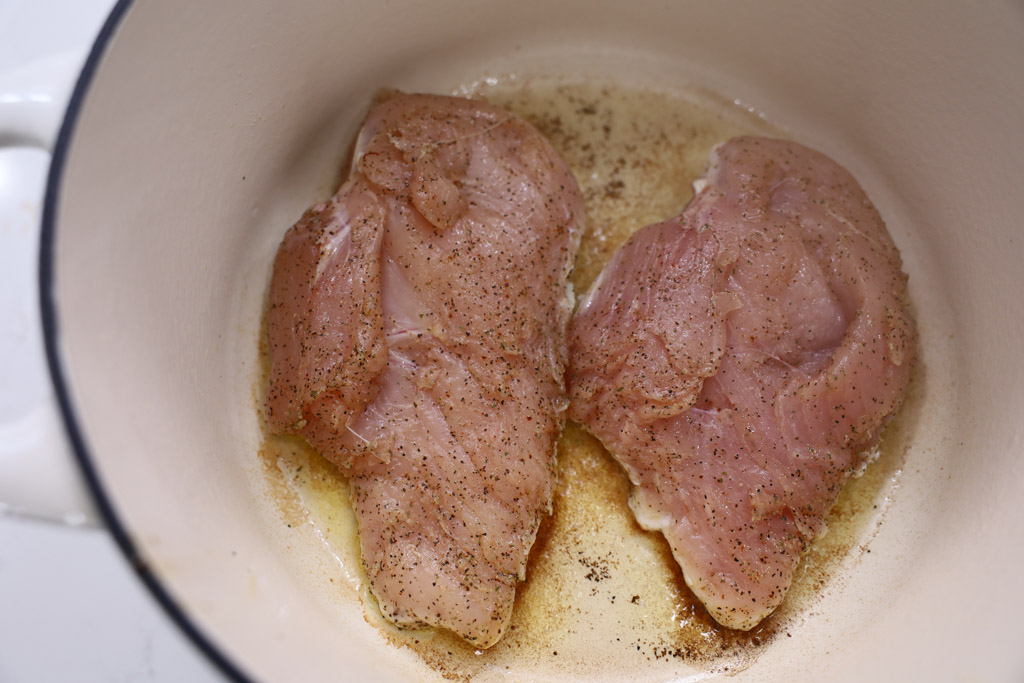 Raw chicken breasts being seared in a pot with avocado oil.