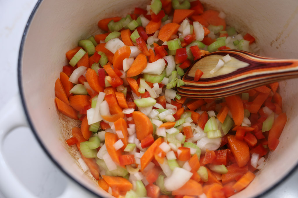 Carrots, celery, and onions being stirred into a pot to form the mirepoix.