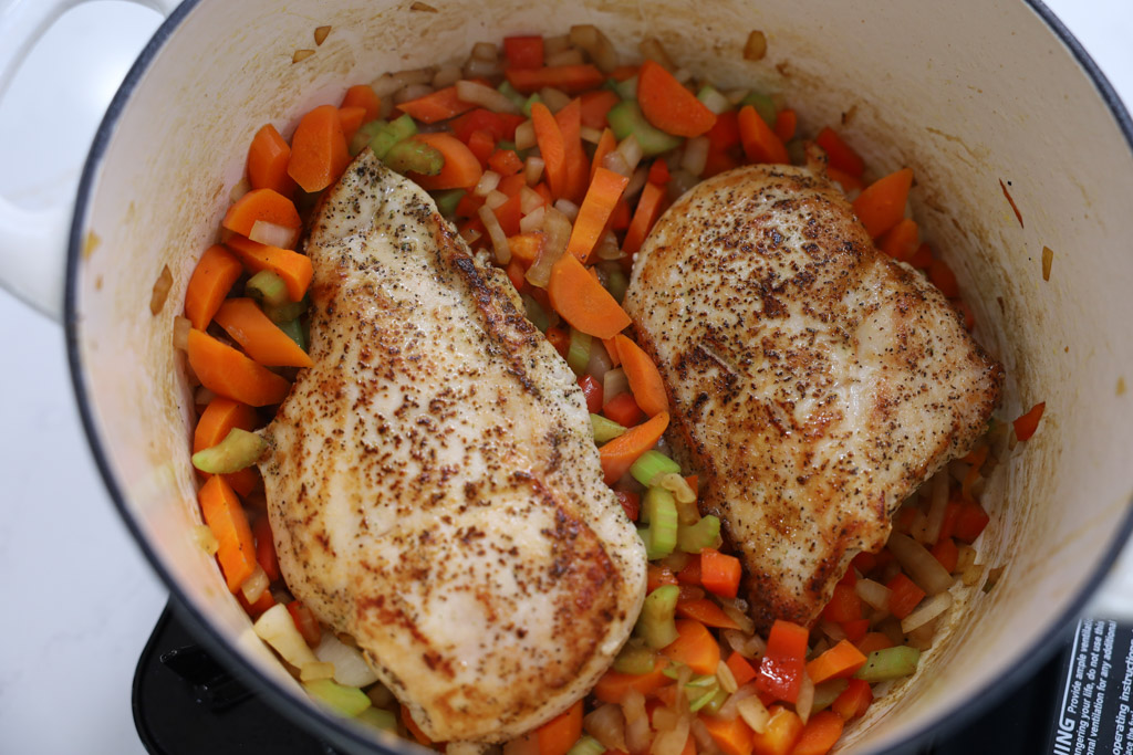 Carrots, onions, celery, and seared chicken breasts in a pot.