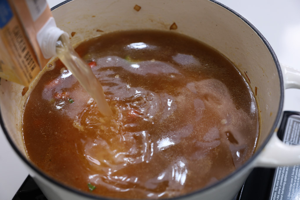 chicken broth being poured into a pot.