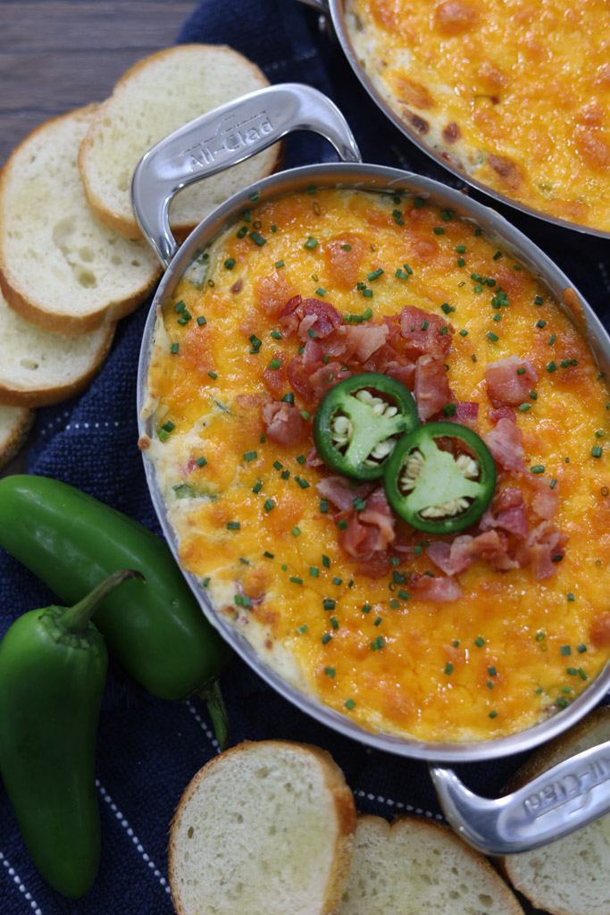 Jalapeno popper dip in a serving dish with crustinis and jalapenos on the side.