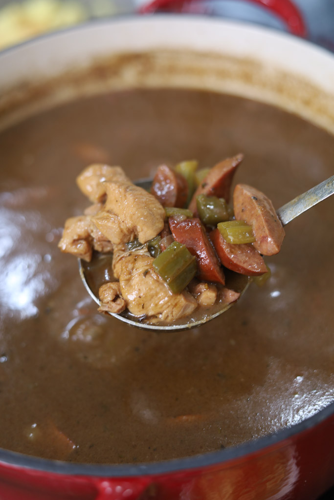 Chicken and Sausage Gumbo in a dutch oven being ladled out to show sausage and chicken.