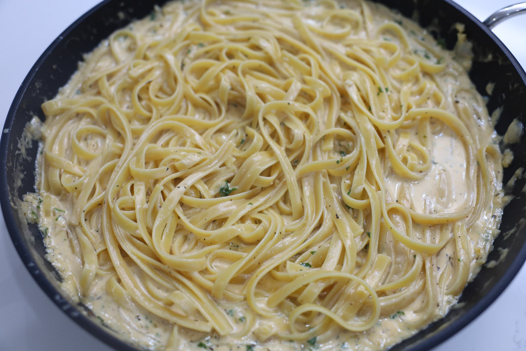 Fettuccine pasta being added into creamy lemon sauce in a saucepan.