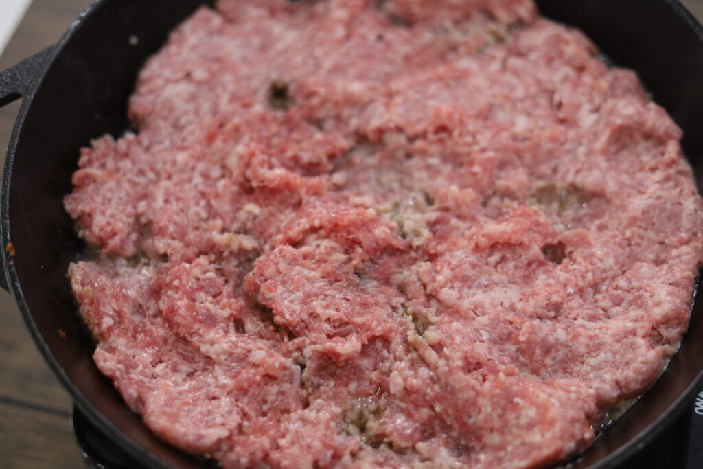 Uncooked sausage in a cast iron, flattened out and cooking to get a nice crust.
