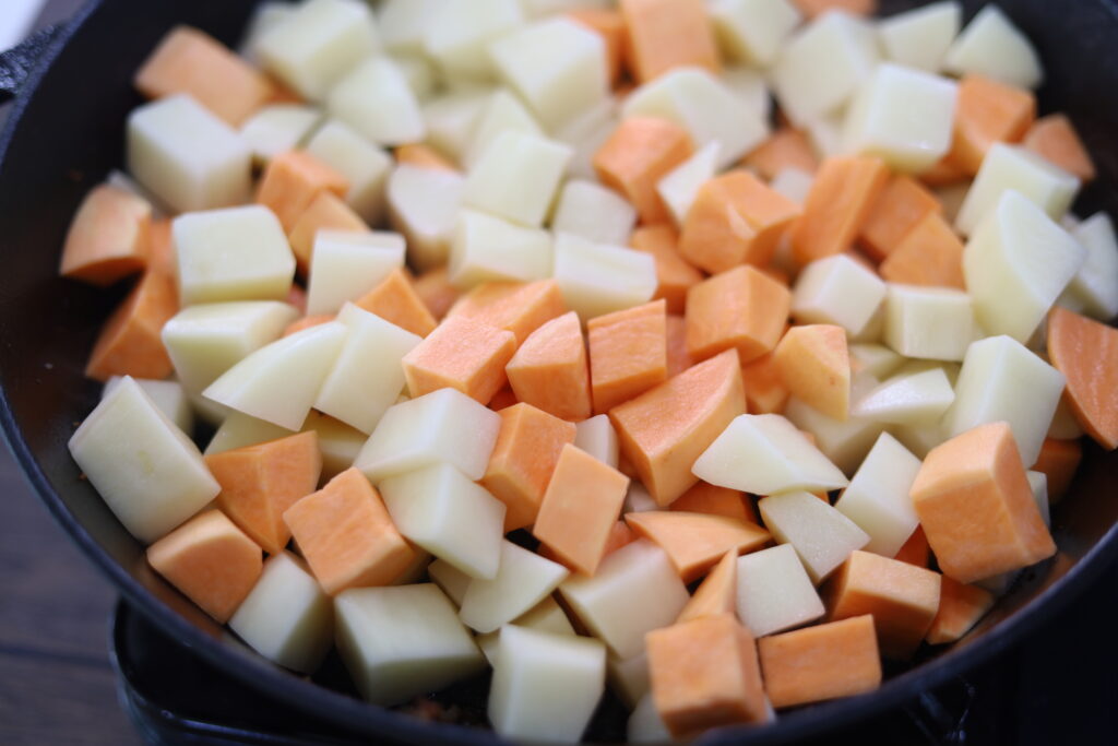 Diced, uncooked sweet potatoes and potatoes in a cast iron.